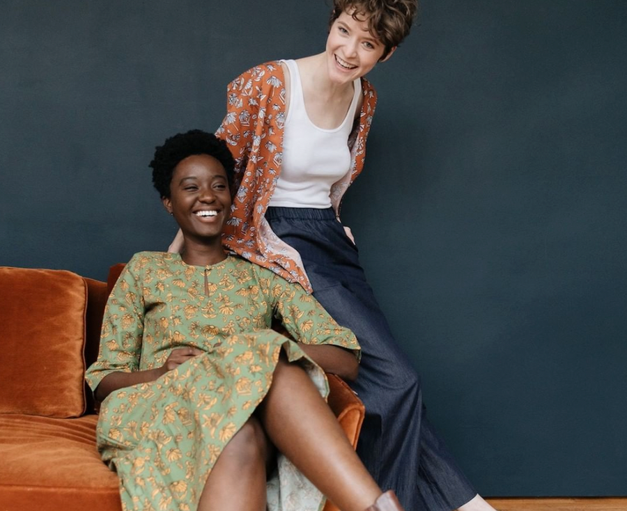 Two women sitting, one in green short sleeve floral maxi dress, the other wearing a white tank top, blue chambray slacks and brown floral jacket. All clothing from wearwell personal stylist subscription membership and made in ethical fair trade facility.