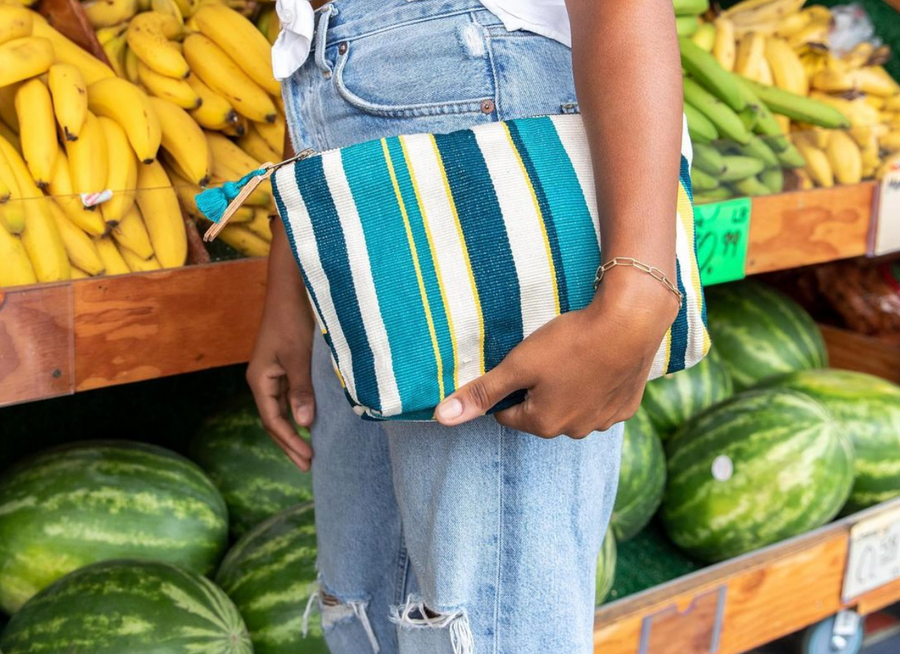Close up of woman in distressed light wash jeans and white linen button down top holding a blue and white striped bag made from handwoven fabric by artisans in a fair trade and ethically run facility.