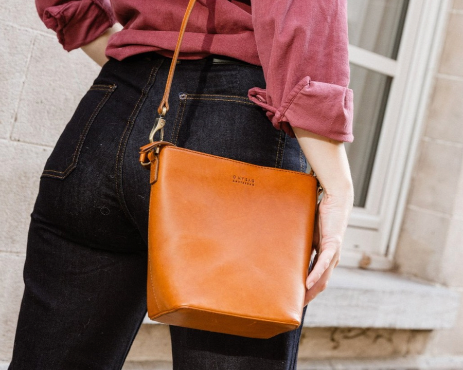 Woman wearing red button down blouse, black jeans, and sustainably made vegetable dyed leather bag with crossbody strap and handle from wearwell personal stylist subscription membership made in ethically run fair trade facility.