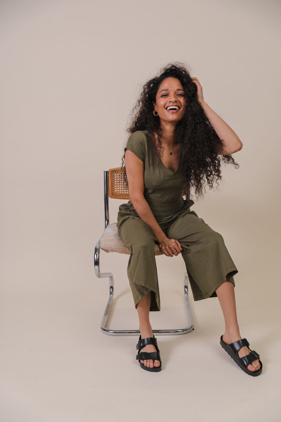 Woman sitting in chair smiling wearing sustainable ethical jumpsuit clothing and vegan accessories from personal styling subscription membership