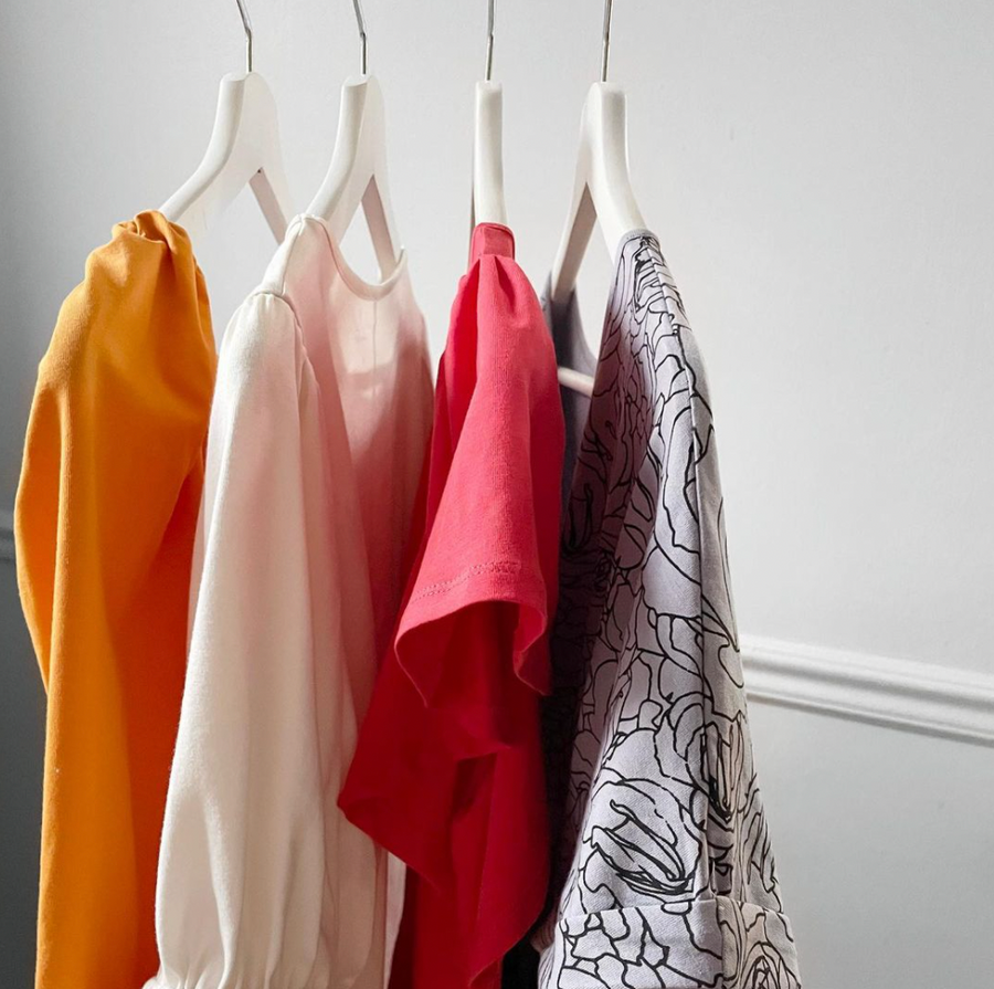 Close up of yellow, white, pink and grey floral short puff sleeve blouses hanging on hangers from a clothing wrack, all available from wearwell personal stylist subscription membership and produced in fair trade facility.