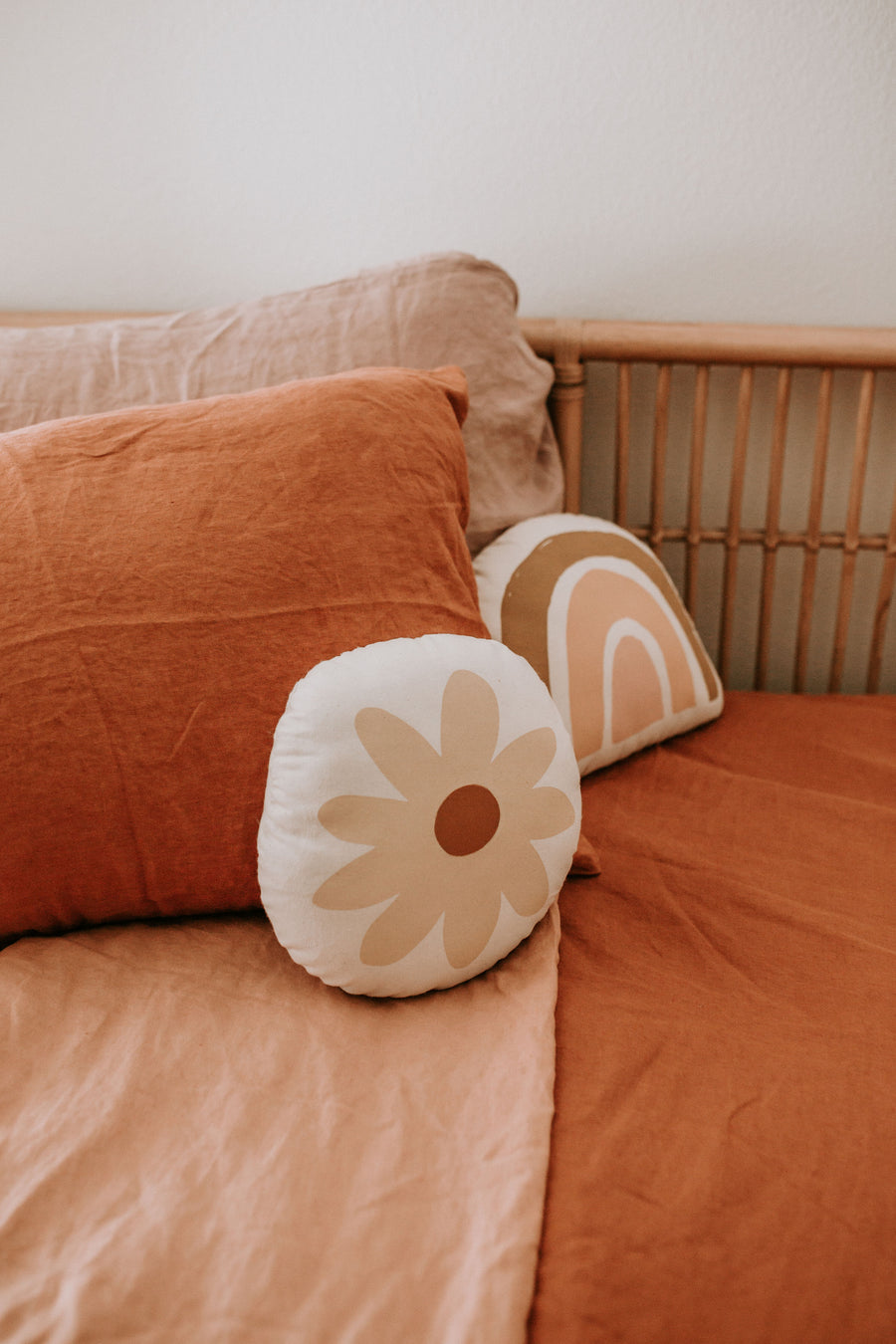 Bed with earth red and peach pillows and sheets with artisan made accent pillows. Accent pillows have rainbow and flower designs. All home goods made at fair trade ethical facility with sustainably sourced materials.