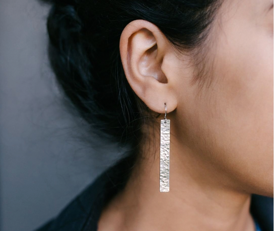 Close up of woman's ear wearing ethical and sustainable hammered silver rectangular pendant earring from wearwell personal stylist subscription membership.