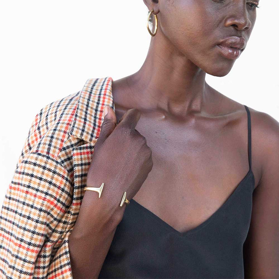 Woman wearing black camisole, gold hoop earrings and brass bracelet, holding plaid blazer. All pieces are sustainable ethical clothing and accessories from wearwell personal stylist subscription membership and made by fair trade artisans.