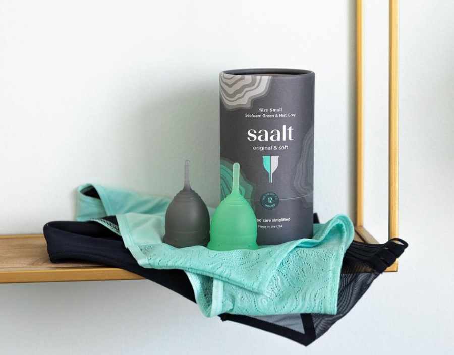 Two menstrual cups, grey and green, on a shelf with two pairs of underwear, teal lace and black mesh. Menstrual cups made with OEKO-TEX certified materials.