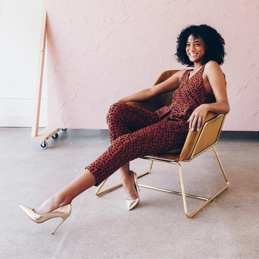Woman sitting wearing a brown leopard print tapered leg jumpsuit and gold heels. She is wearing sustainable ethical clothing and accessories from wearwell personal stylist subscription membership and produced in fair trade ethically run facility.