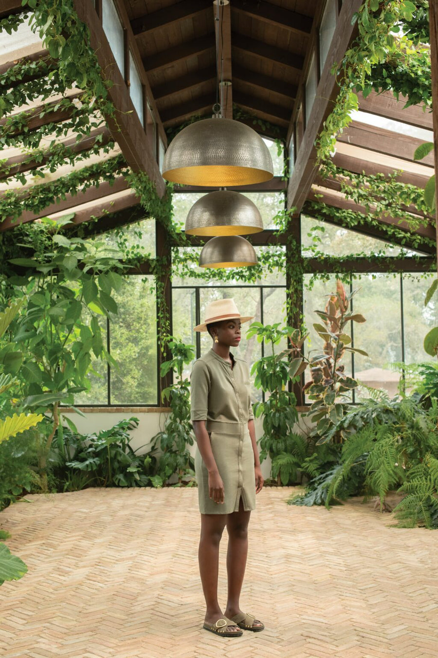Woman standing in greenhouse wearing green cotton jersey dress, straw hat, and sandals. All are sustainable ethical clothing and accessories from wearwell personal stylist subscription membership and produced in fair trade ethically run facilities..