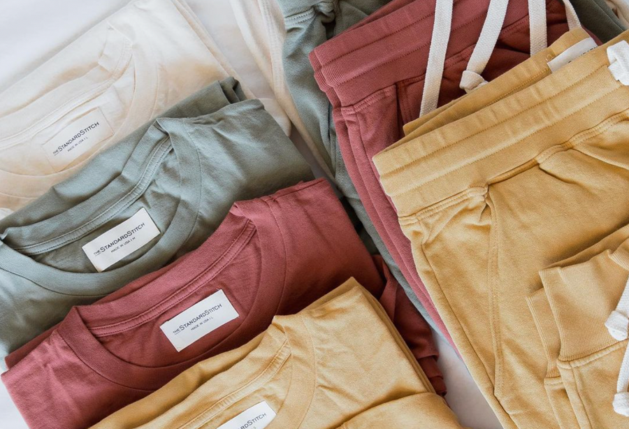 Sustainably made, non-toxic dyed, t-shirts and joggers in white, green, red and yellow laying on a table. All are sustainable ethical clothes from wearwell personal stylist subscription membership and made in fair trade facility.