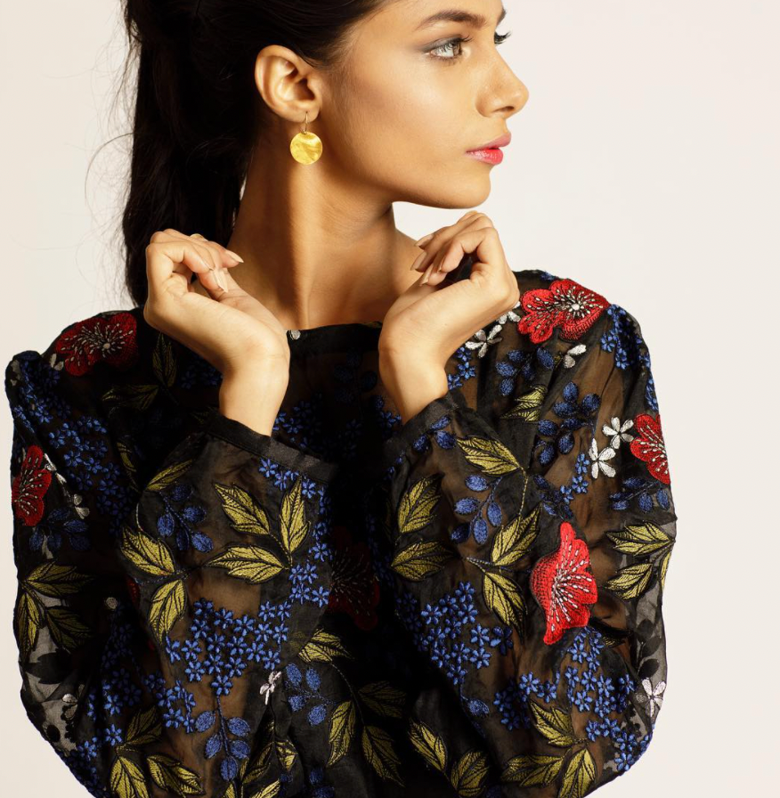 Woman wearing gold drop earrings and black blouse with hand embroidered multi color floral detail from wearwell personal stylist subscription membership, made with sustainably sourced materials in ethically run fair trade facility.