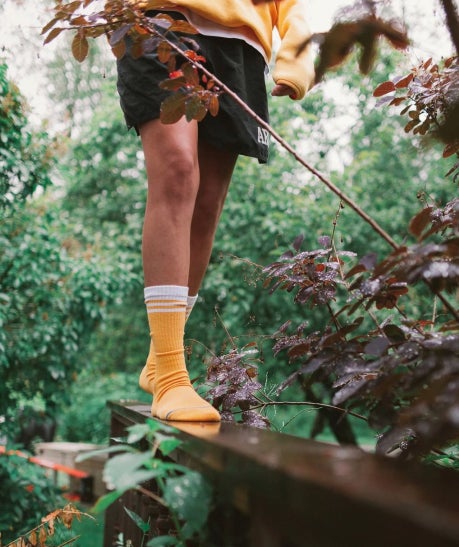 Person walking outdoors wearing yellow and white sustainably made cotton socks, black jersey shorts and yellow sweatshirt, all ethical clothing and accessories from wearwell personal stylist subscription membership.