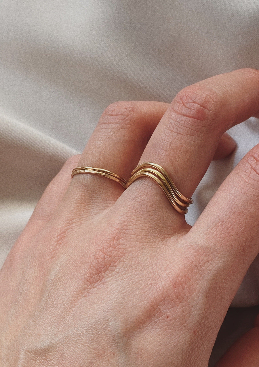 A model is wearing three gold Curve Rings on her middle finger. She is also wearing two gold Simple Stacking Rings on her ring finger. This is a lifestyle photo of the Curve Ring.
