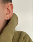 The model is wearing two pairs of the Ear Hugger Hoops in gold. One pair is smooth while the other is beaded. The model is wearing an olive green sweater.