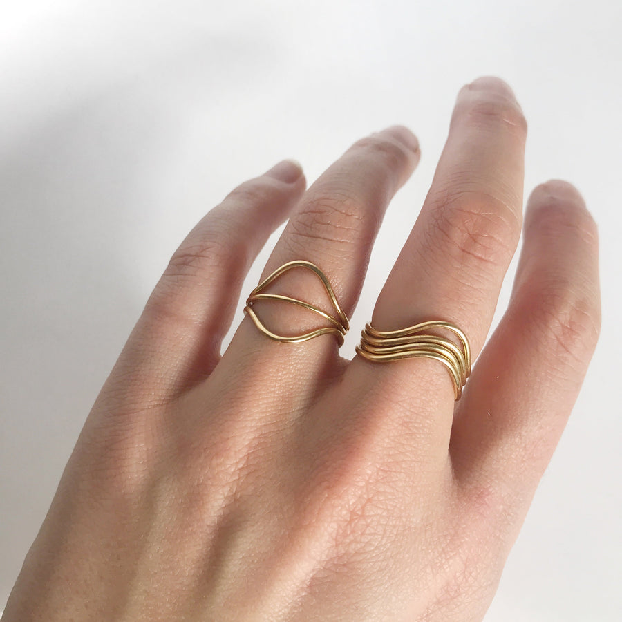 The model is wearing two Curve Rings and a Simple Stacking Ring on her ring finger. She's also wearing three curve rings sitting in the same way on her middle finger. All of the rings are gold.